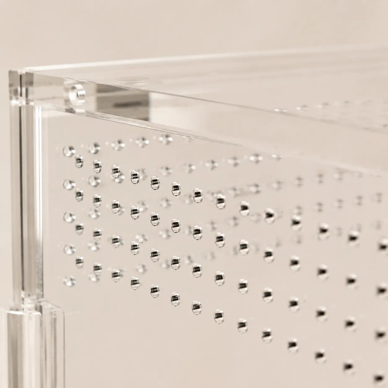 Macro close-up of the rows of small round laser-cut ventilation holes in a clear acrylic enclosure panel
