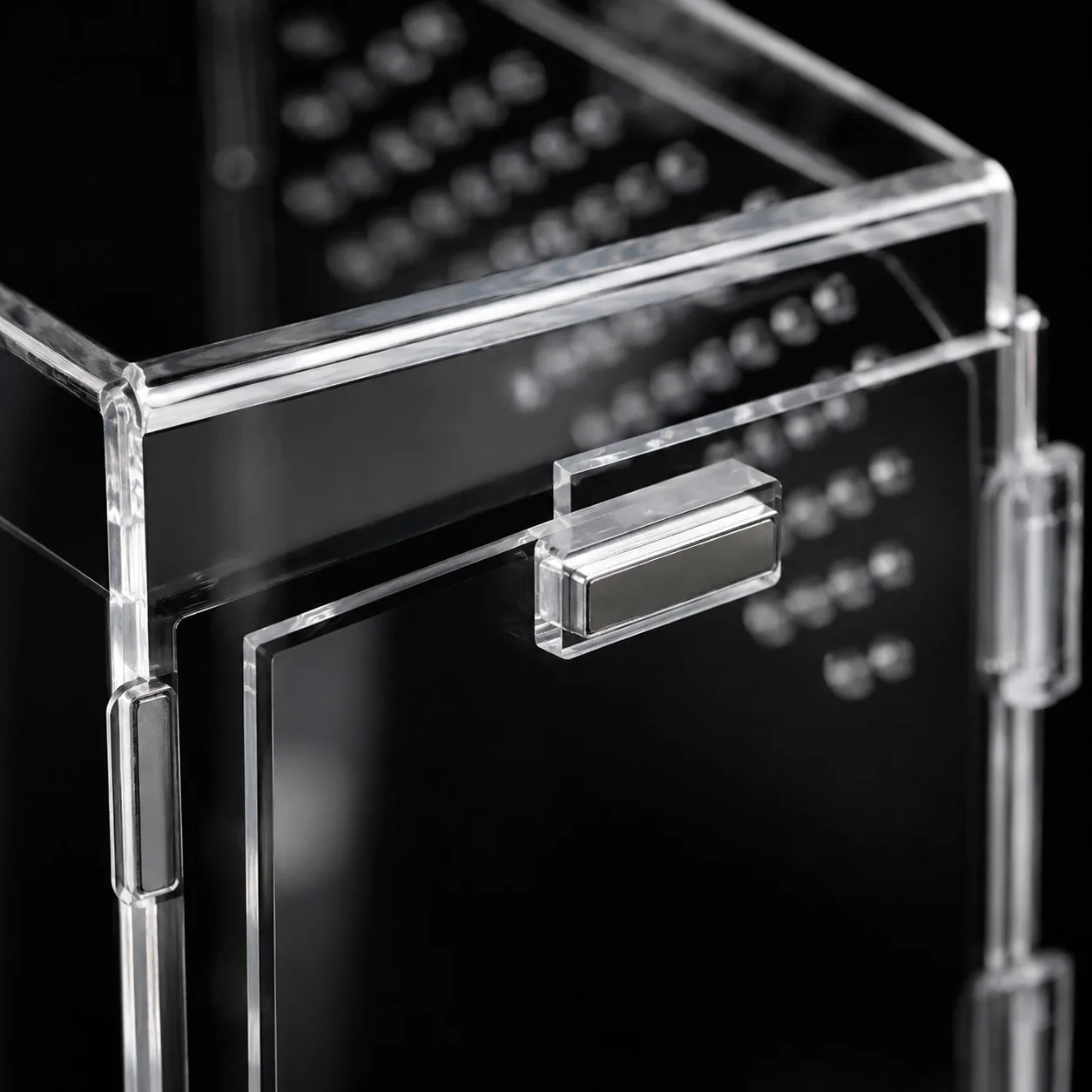 Close-up of the flush magnetic lid bar and its silver magnet strip on the corner of a clear acrylic enclosure against a black background